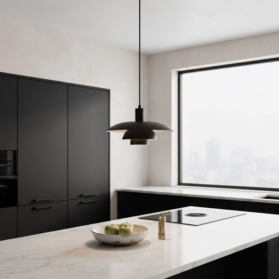 A modern black pendant light with a layered disc design hangs over a white marble kitchen island in a minimalist kitchen setting.