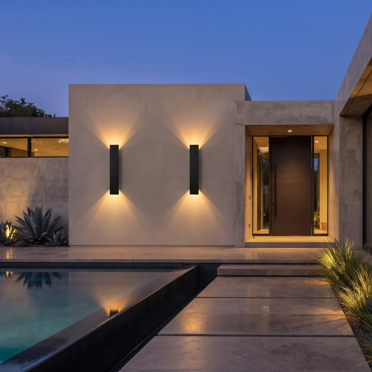 Two modern black rectangular wall sconces mounted on a beige stucco house exterior at dusk, casting warm light onto the wall and reflecting onto a swimming pool.