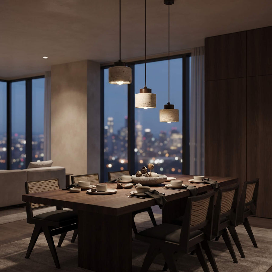 A modern dining room interior with a dark wood rectangular dining table surrounded by matching chairs, set with white tableware. Three pendant lights hang above the table, and large windows behind show a city skyline at dusk.