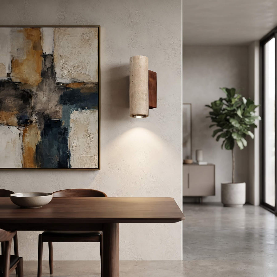 A modern cylindrical wall sconce with a textured beige fabric shade and a dark wood backplate, mounted on a textured plaster wall in a minimalist dining room setting.