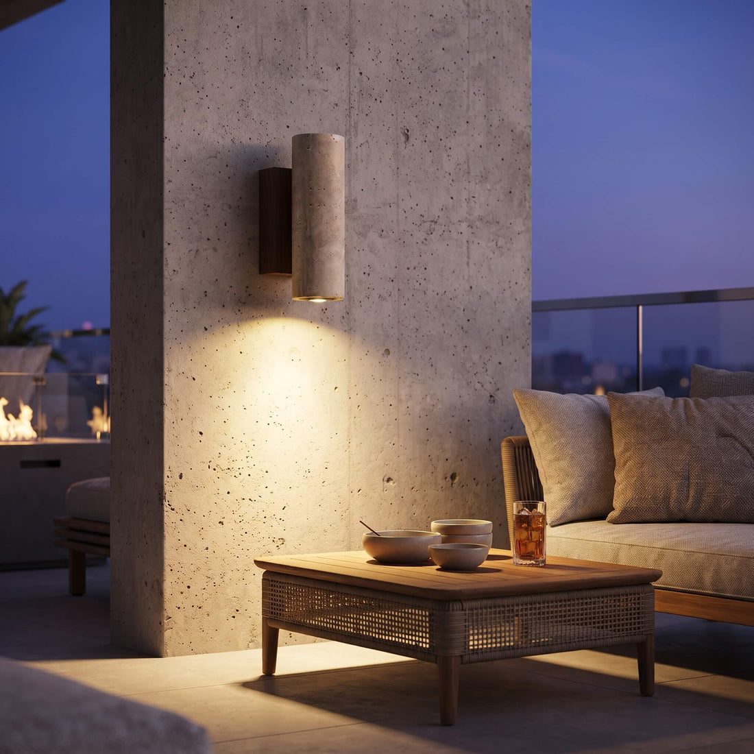 A modern cylindrical wall sconce with a textured beige fabric shade and a dark wood backplate, mounted on a cement wall in a balcony setting