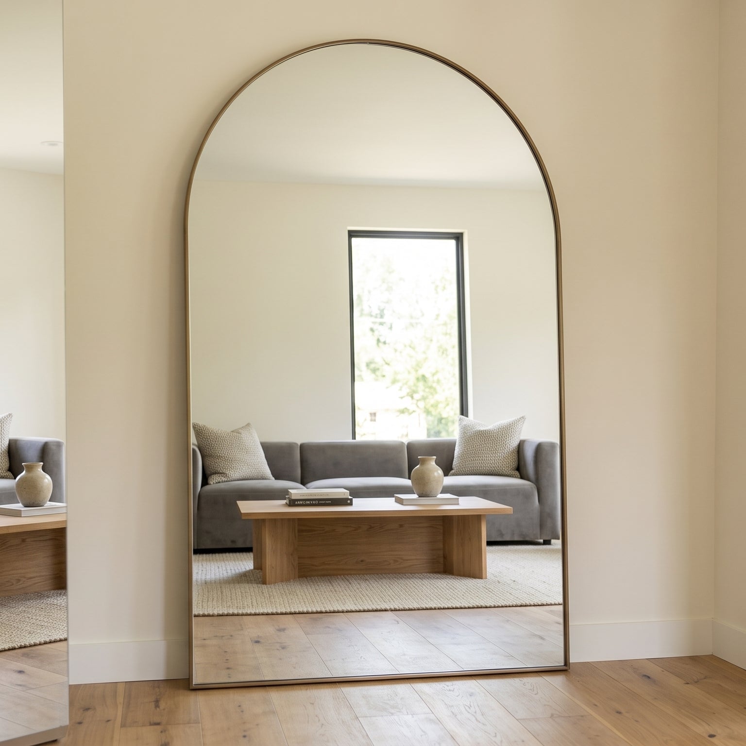 Living room with a large arch-shaped mirror reflecting a gray sofa and coffee table.