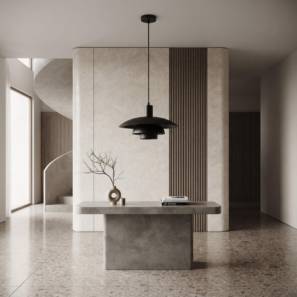 A modern black pendant light with a layered, saucer-like shade hangs over a minimalist concrete console table in a contemporary interior with textured beige walls and wood slat accents.