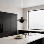 A modern black pendant light with a layered disc design hangs over a white marble kitchen island in a minimalist kitchen setting.