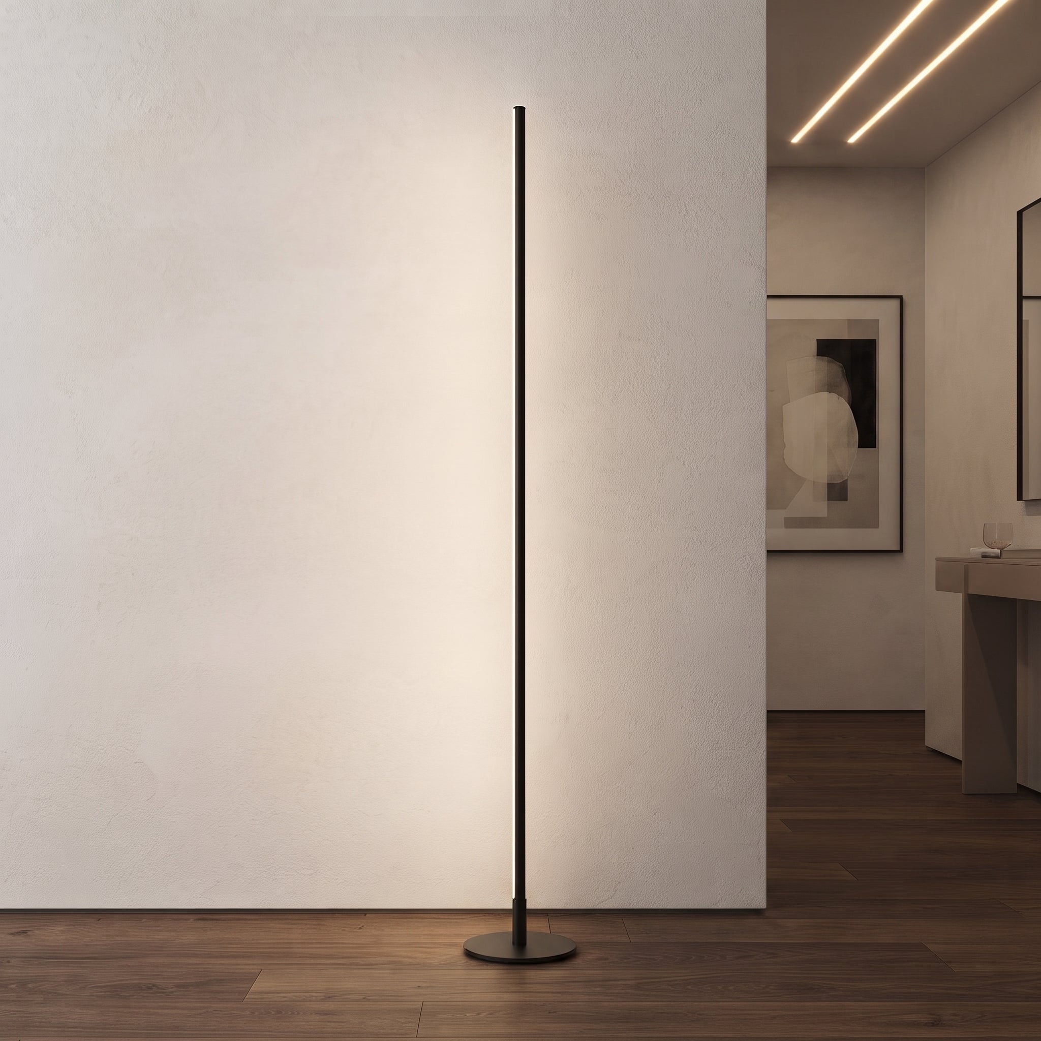 A slim black floor lamp with a circular base stands on a dark wood floor against a white wall in a modern interior hallway.