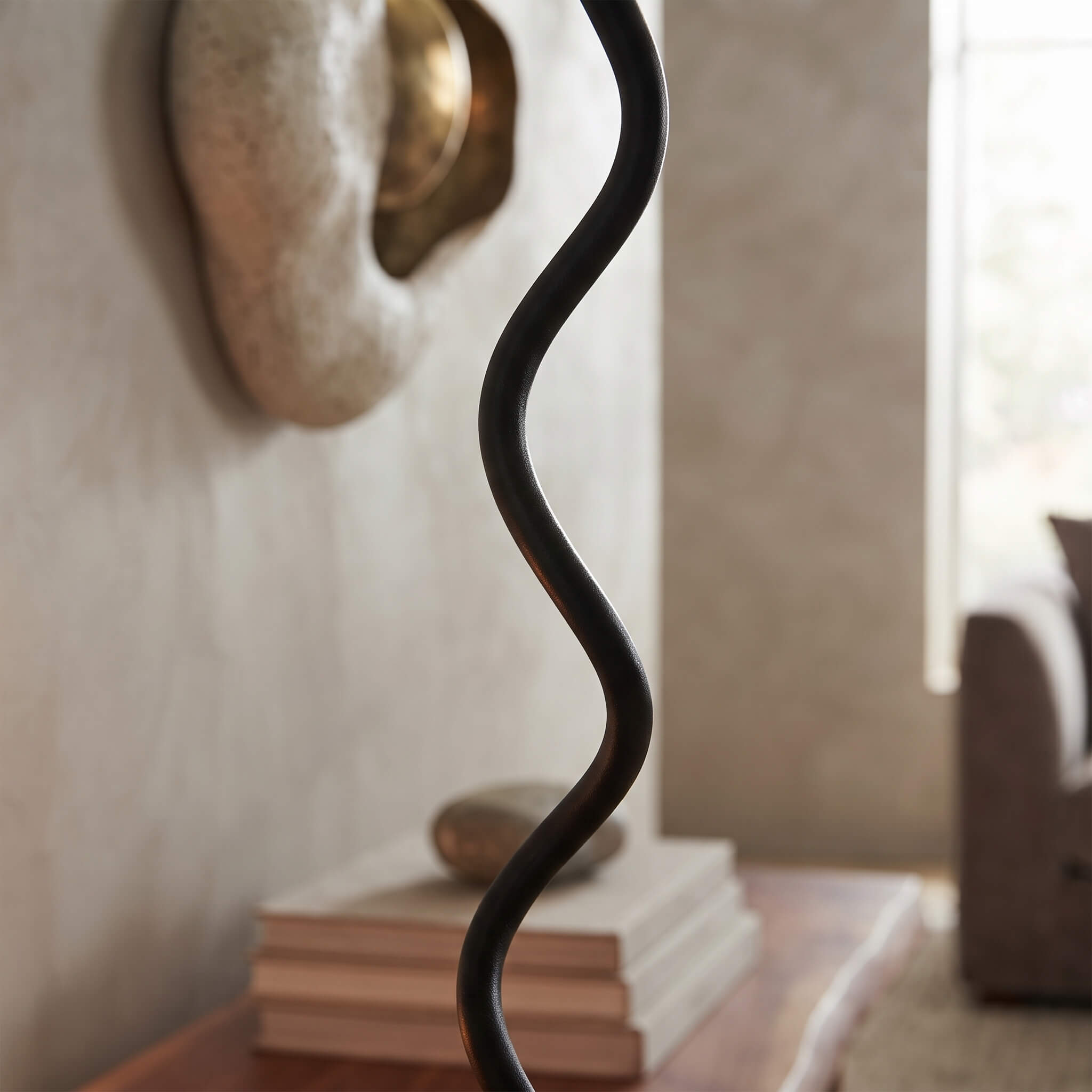 A close-up of a black metal floor lamp with a wavy, sculptural cord-like shade in a softly lit living room setting.