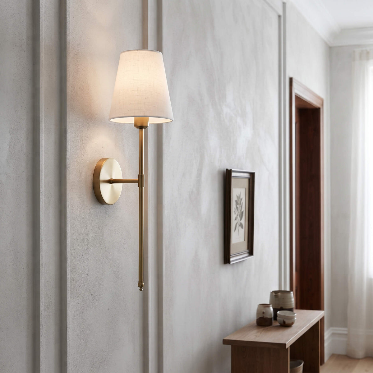 Brass wall sconce lighting a hallway beside a framed botanical print