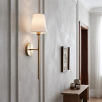 Brass wall sconce lighting a hallway beside a framed botanical print