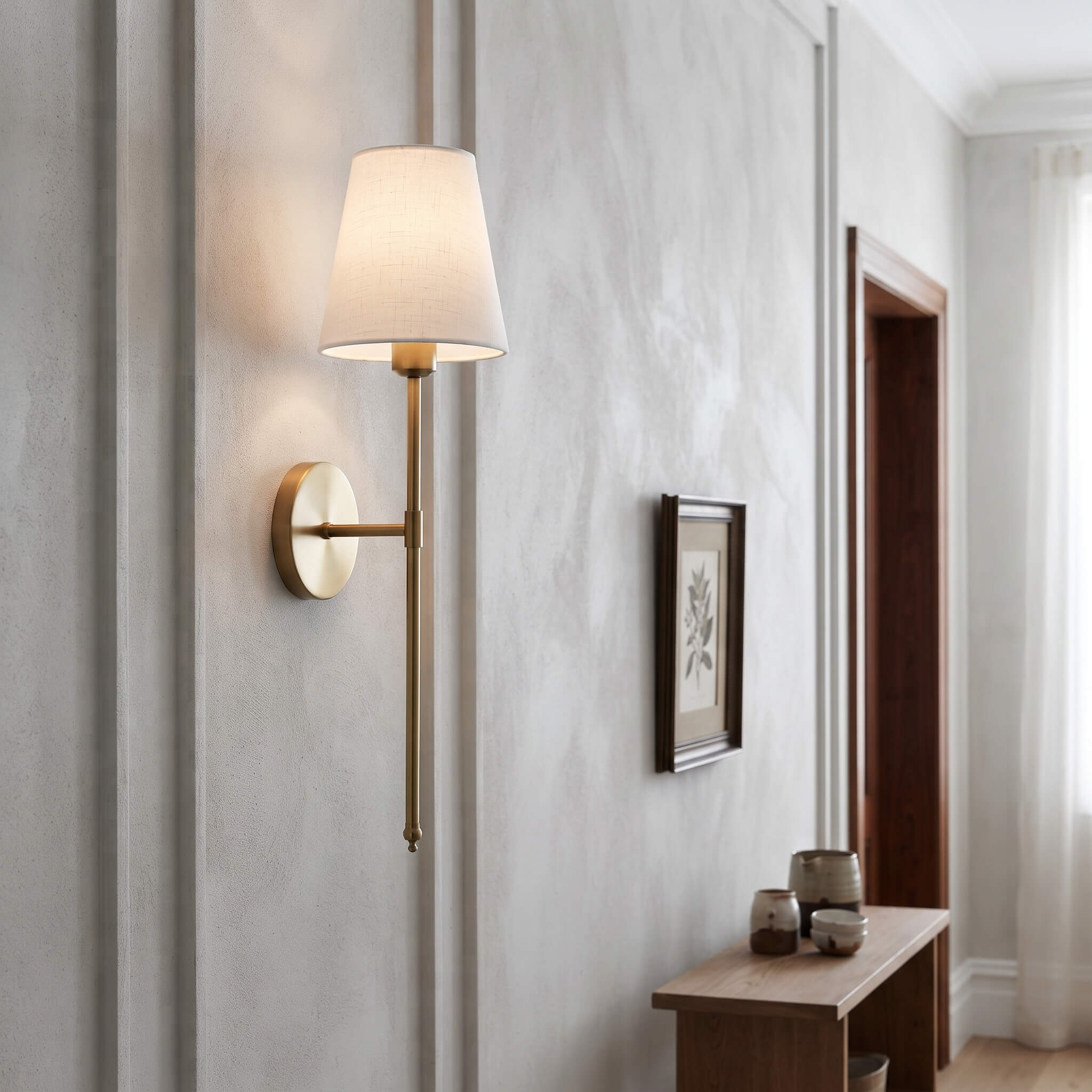 Brass wall sconce lighting a hallway beside a framed botanical print