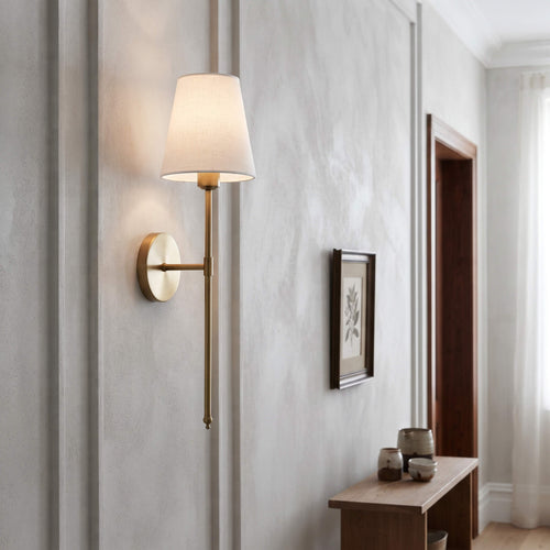 Brass wall sconce lighting a hallway beside a framed botanical print