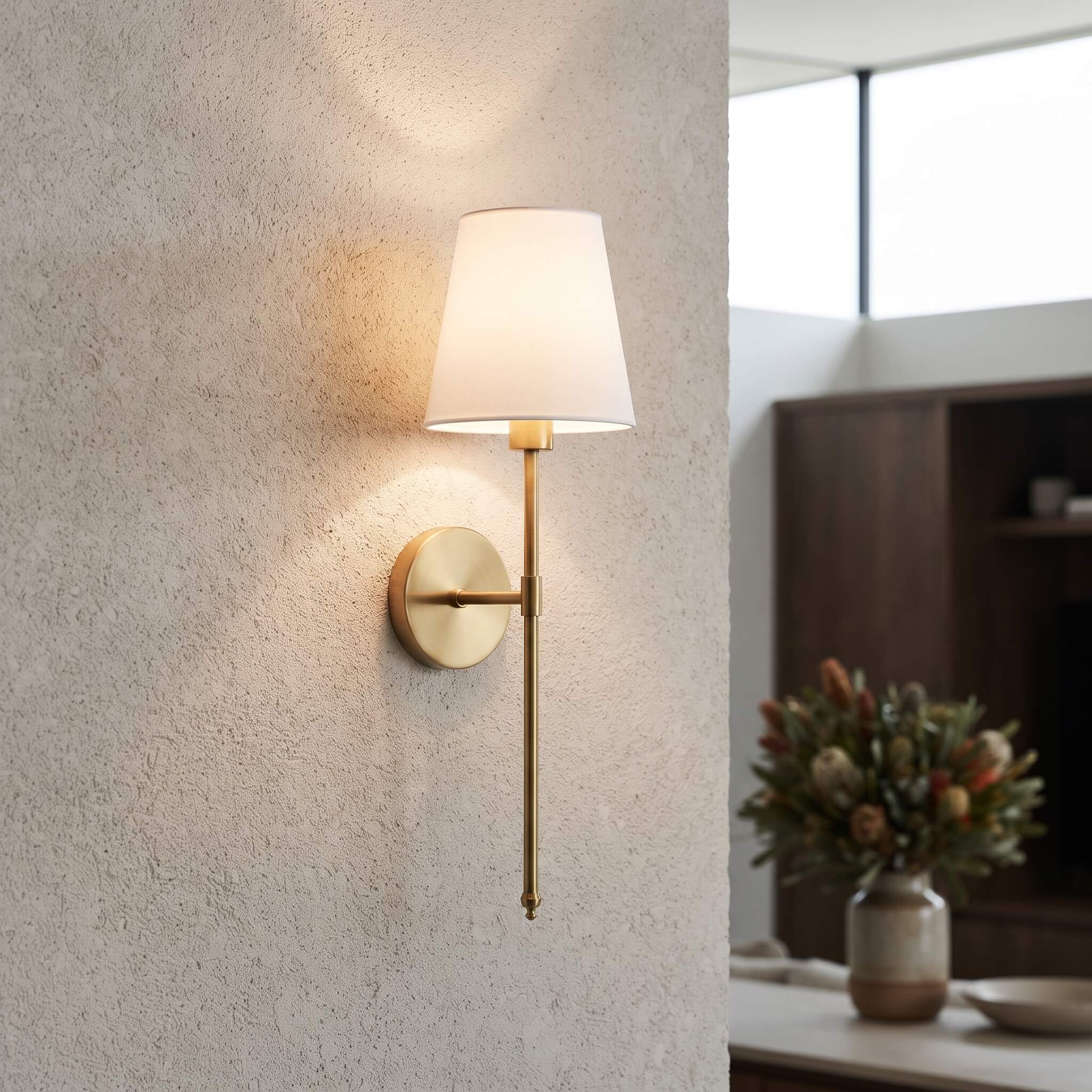 Brass finish wall sconce glowing against a textured plaster wall