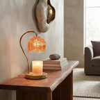 A warm amber glass table lamp with a curved brass stand and a lit candle on a wooden console table in a cozy living room setting.