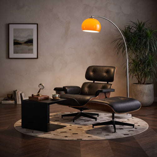 A modern lounge chair with an attached ottoman in black leather and wood, styled in a warm, dimly lit room with a glowing orange floor lamp, a side table, and a potted plant.