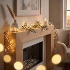 Warm white LED fairy string lights draped over a wooden fireplace mantel in a cozy living room setting, alongside a white vase with dried grass, a lit candle, and green garland.