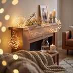 Warm white LED string lights draped around a wooden fireplace mantel in a cozy living room setting, with candles, a framed print, and a knitted blanket visible.