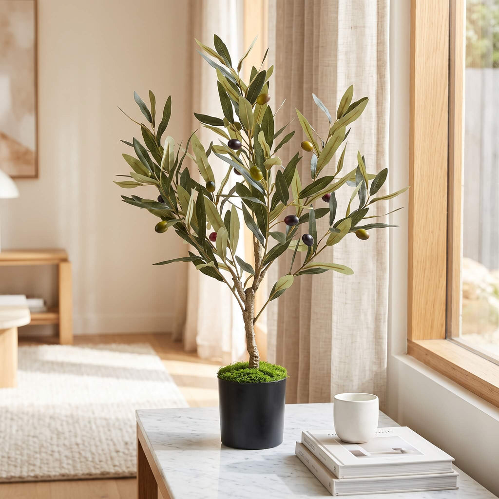 Realistic faux olive tree 60cm in black pot with moss detail, styled on marble table beside window