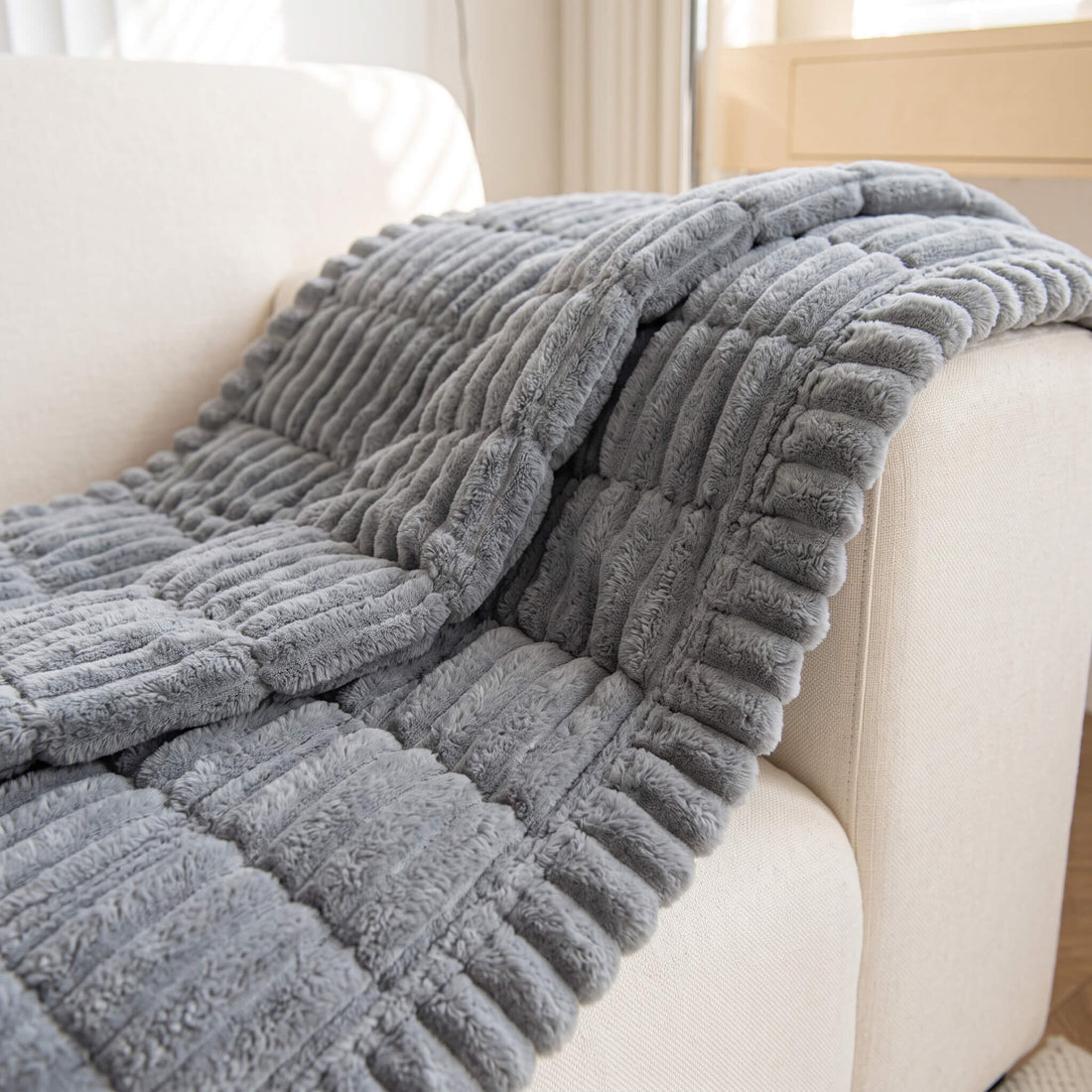Grey quilted sofa cover draped over a curved sofa arm
