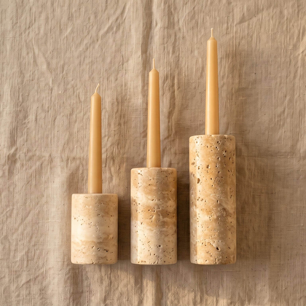 Three taper candles in matching cylindrical stone holders of graduated sizes, displayed on a textured beige linen background.