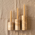Three taper candles in matching cylindrical stone holders of graduated sizes, displayed on a textured beige linen background.