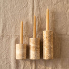 Three taper candles in matching cylindrical stone holders of graduated sizes, displayed on a textured beige linen background.