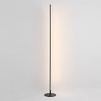 A modern slim floor lamp with a dark metal circular base and a long vertical rod emitting a warm light, shown against a plain light gray background.