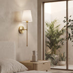 Brass wall sconce above an oak nightstand in a light filled bedroom