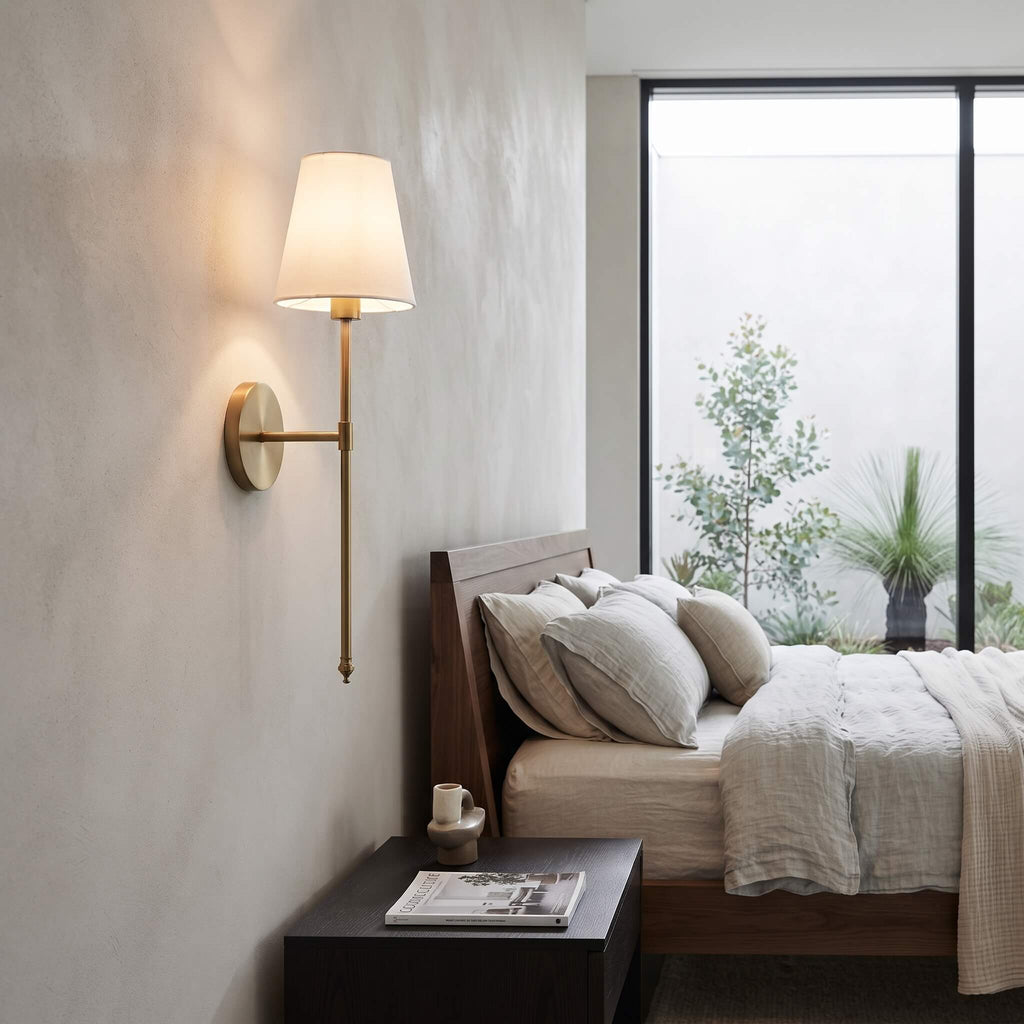 Brass wall sconce lit above a bedside table in a modern bedroom