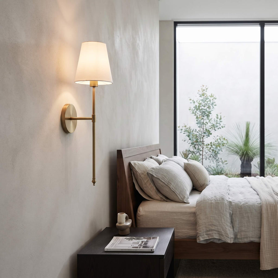 Brass wall sconce lit above a bedside table in a modern bedroom