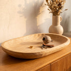 Wooden bowl on a wooden surface with keys and a small ball, with a vase of dried flowers in the background.