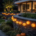 Solar pumpkin lantern string lights glowing along a stone garden wall at dusk