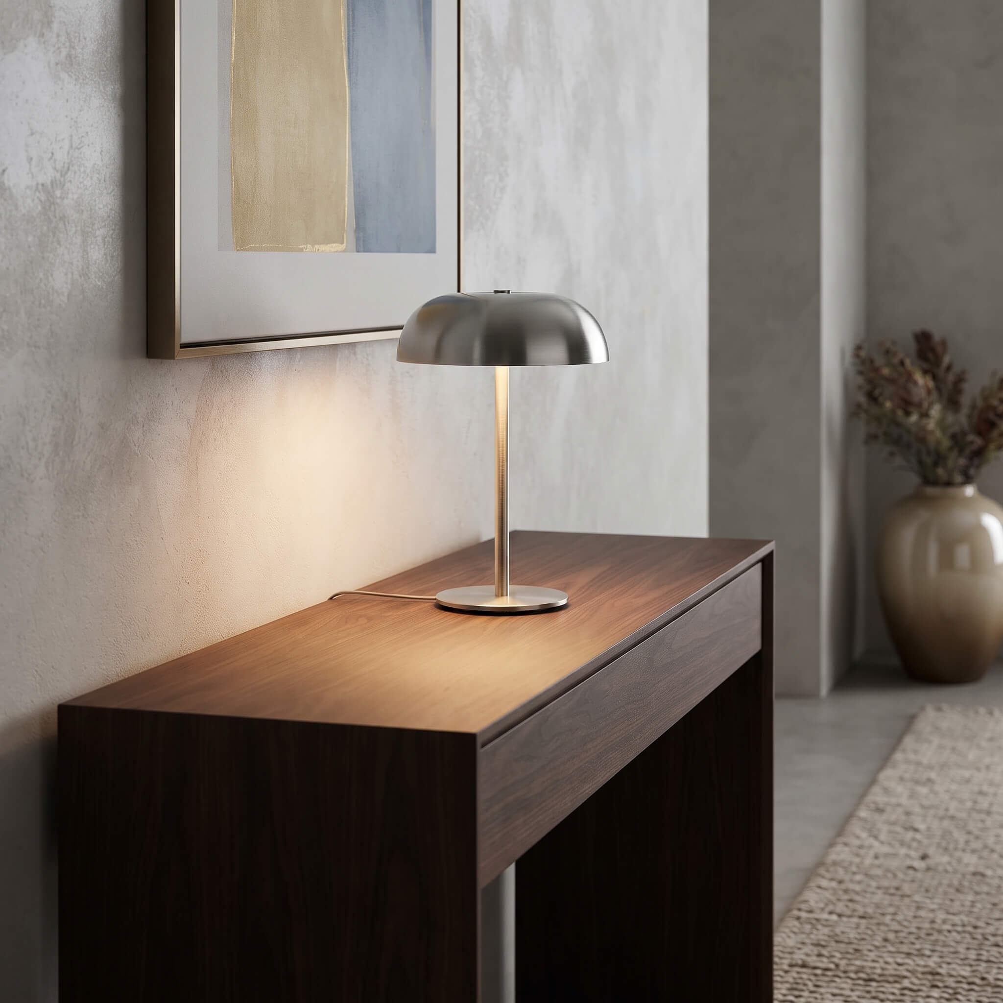 A modern table lamp with a brushed silver dome shade and a gold-toned stem sits on a dark wood console table in a minimalist interior setting.