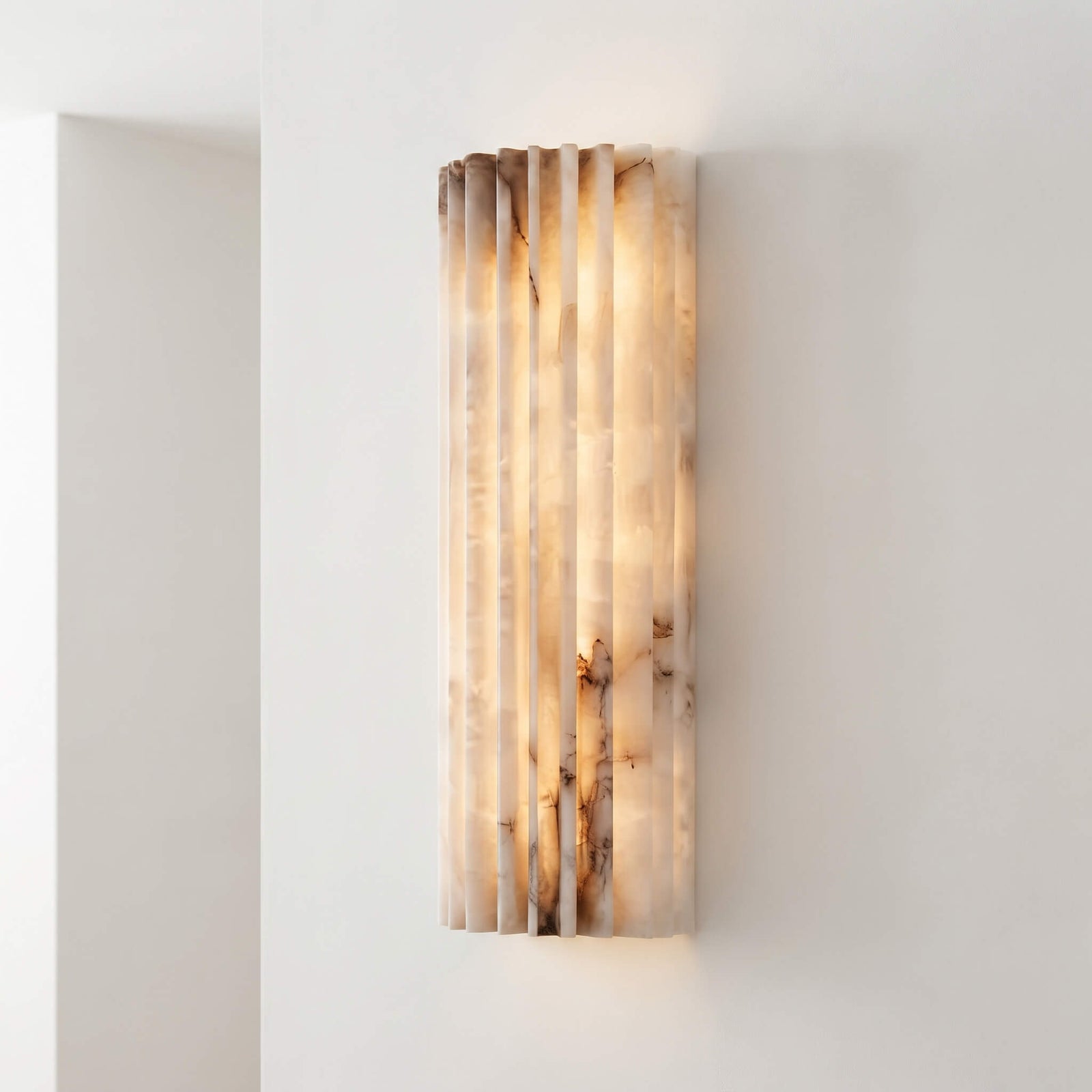 Fluted alabaster wall sconce lit against a white wall