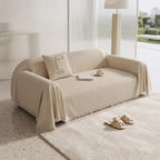 Beige sofa cover throw with the fringed edge pooling onto a rug