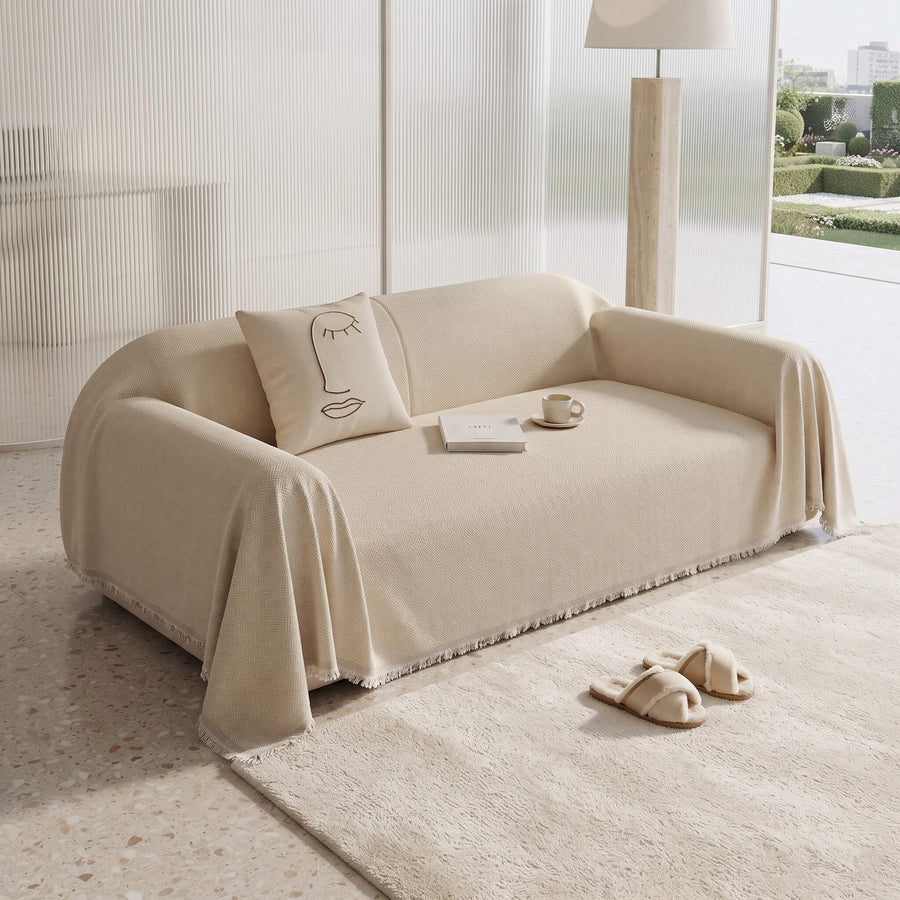 Beige sofa cover throw with the fringed edge pooling onto a rug