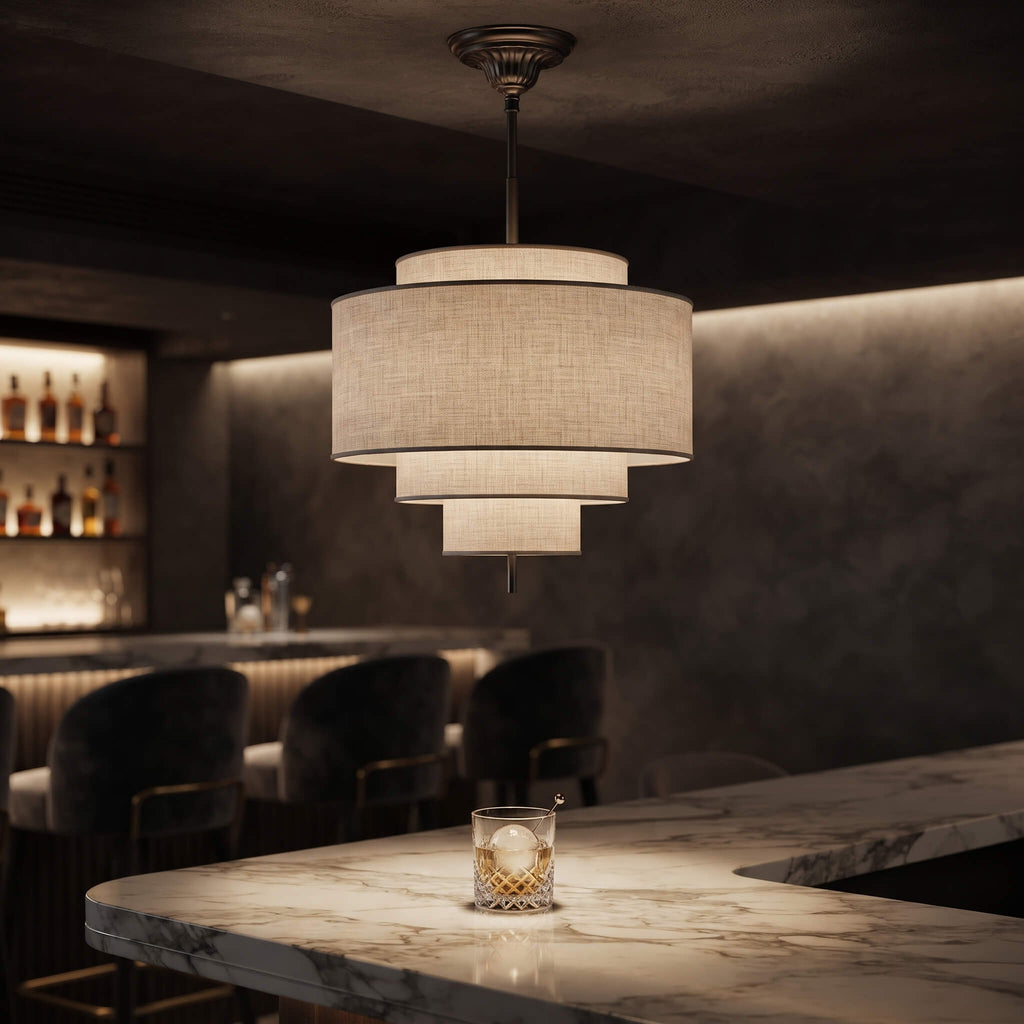 A modern three-tier pendant light with a textured beige linen shade hangs over a marble bar counter in a dimly lit bar setting.
