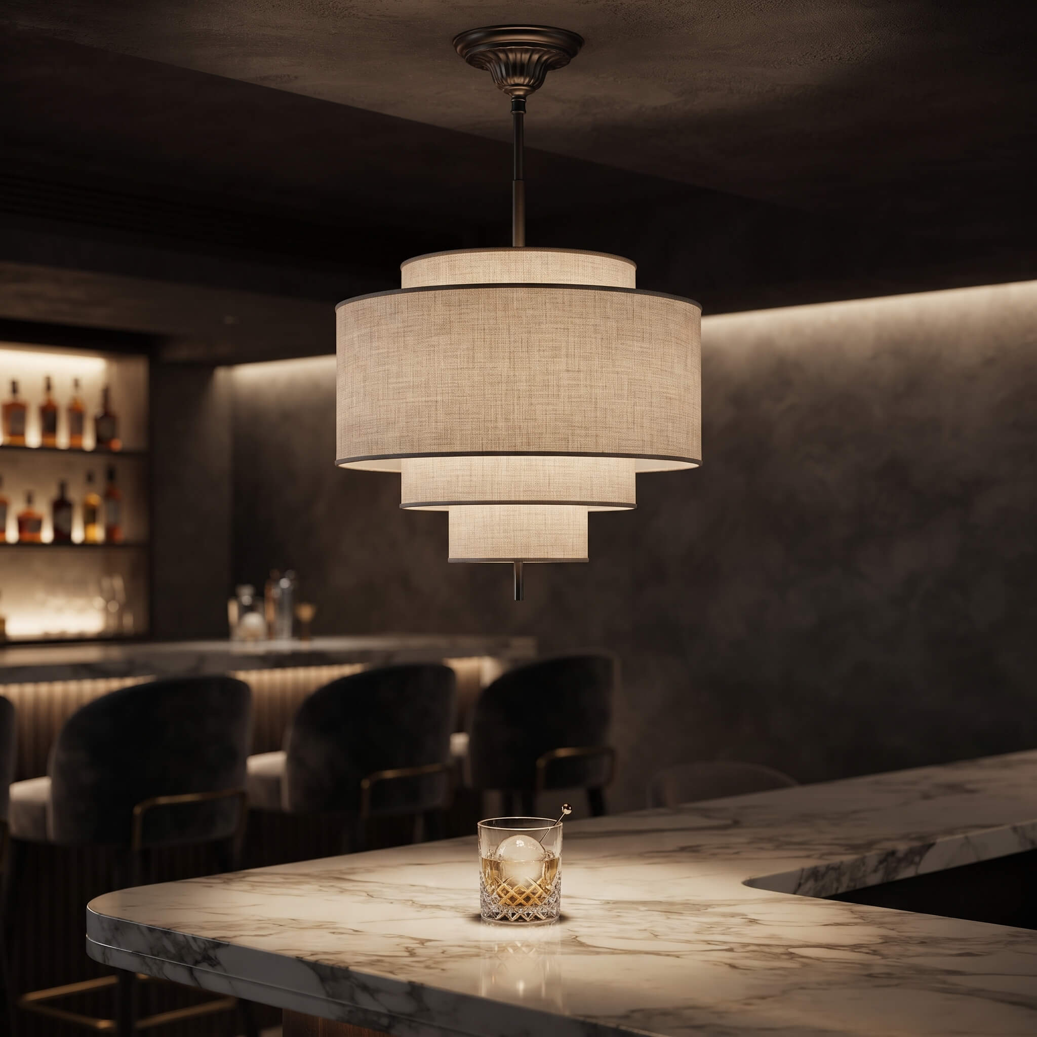 A modern three-tier pendant light with a textured beige linen shade hangs over a marble bar counter in a dimly lit bar setting.