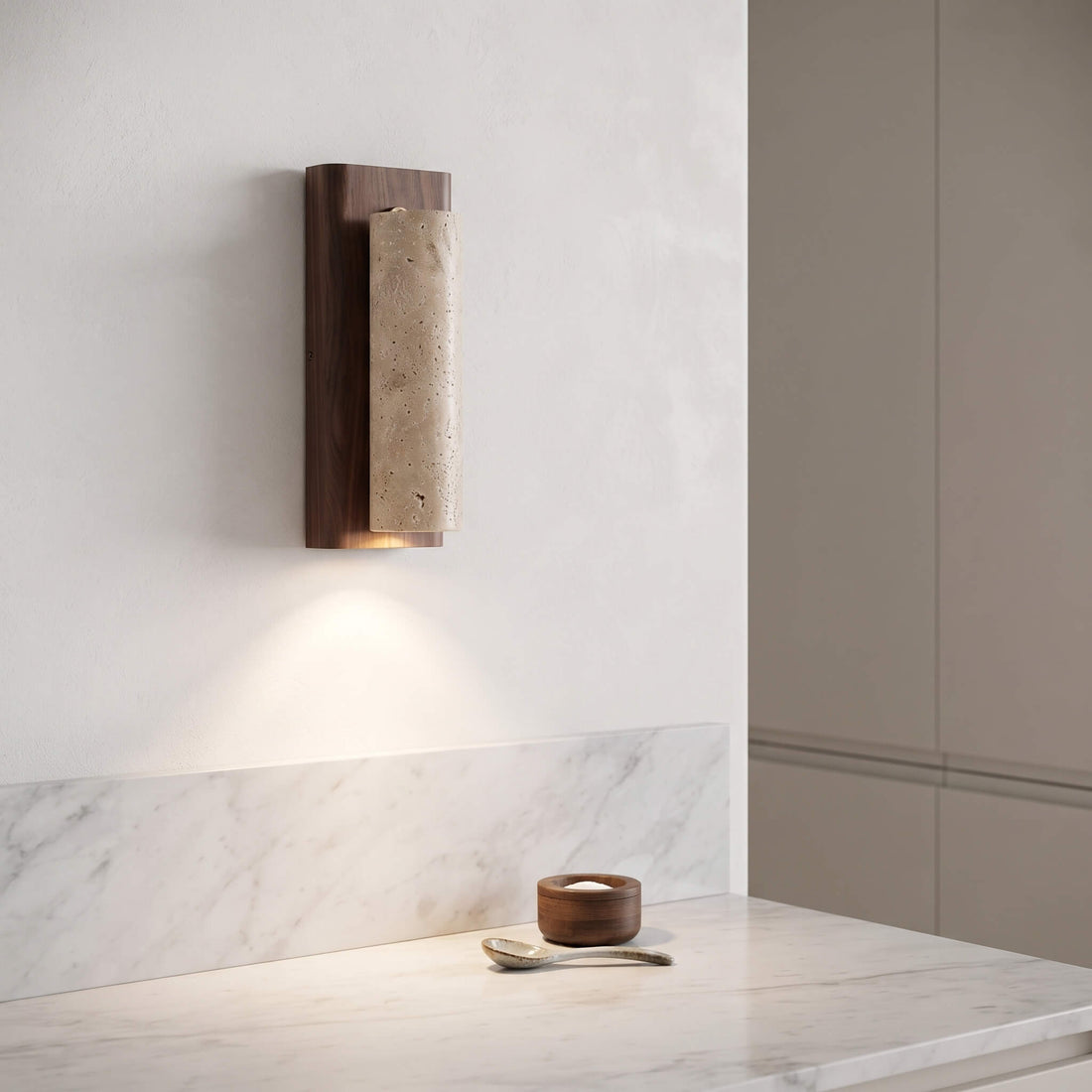 A modern wall sconce with a dark wood frame and a textured beige stone cylinder, mounted on a white wall above a marble countertop.