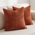 Two square rust-orange corduroy throw pillows with a patchwork design, styled on a light beige sofa.