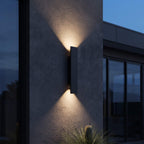 Matte black up and down outdoor wall sconce casting warm light across an exterior wall
