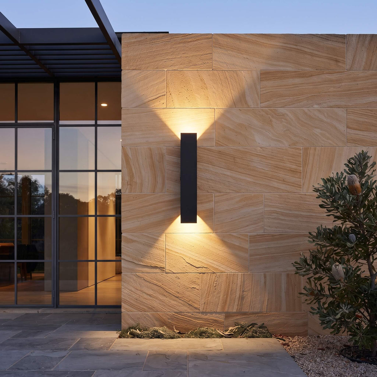 Close view of the matte black outdoor wall sconce casting warm light up and down a rendered wall