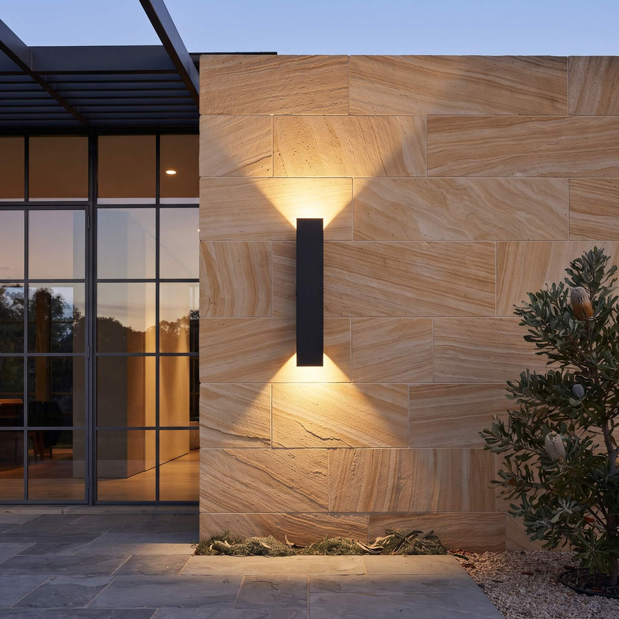 Close view of the matte black outdoor wall sconce casting warm light up and down a rendered wall