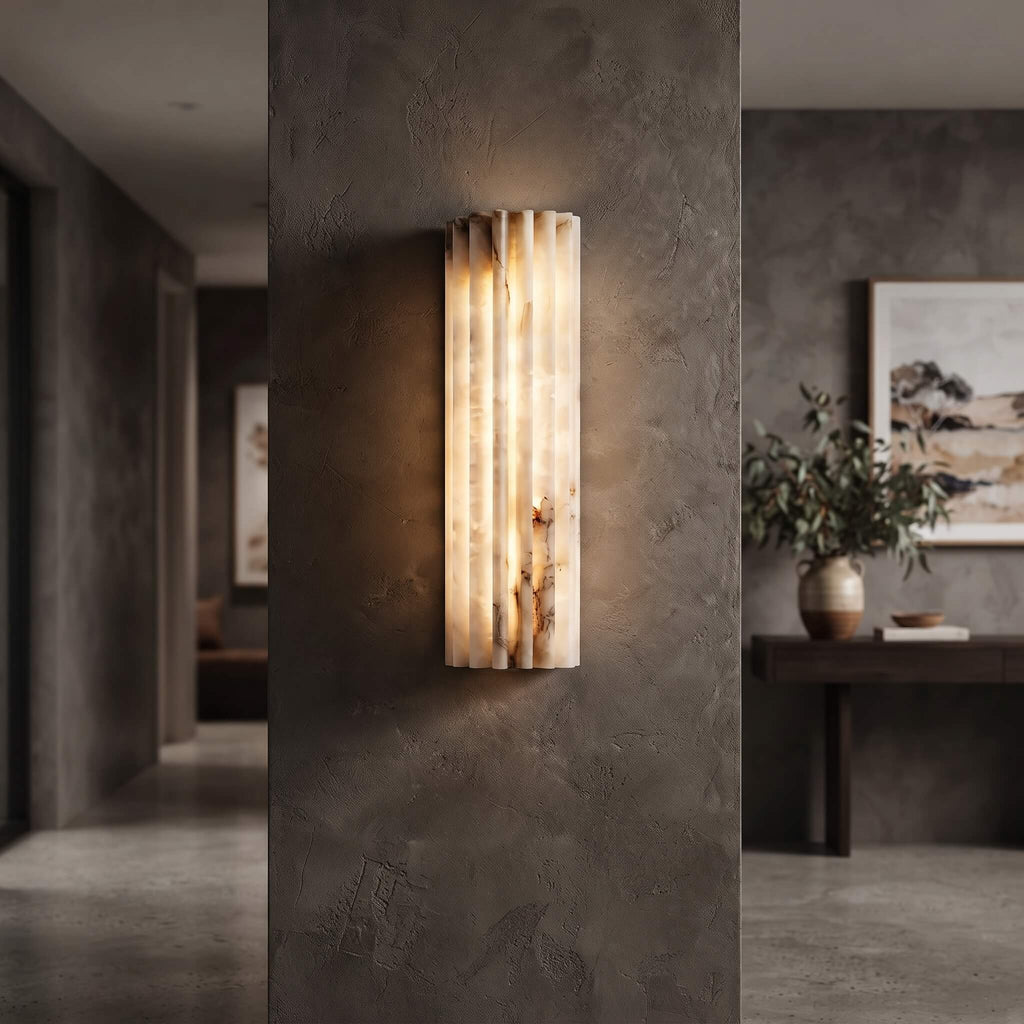 Fluted profile of the alabaster sconce glowing on a dark plaster wall