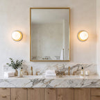 Globe wall sconces flanking a gold framed mirror above a marble vanity