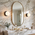 Pair of opal glass globe wall sconces flanking an oval bathroom mirror