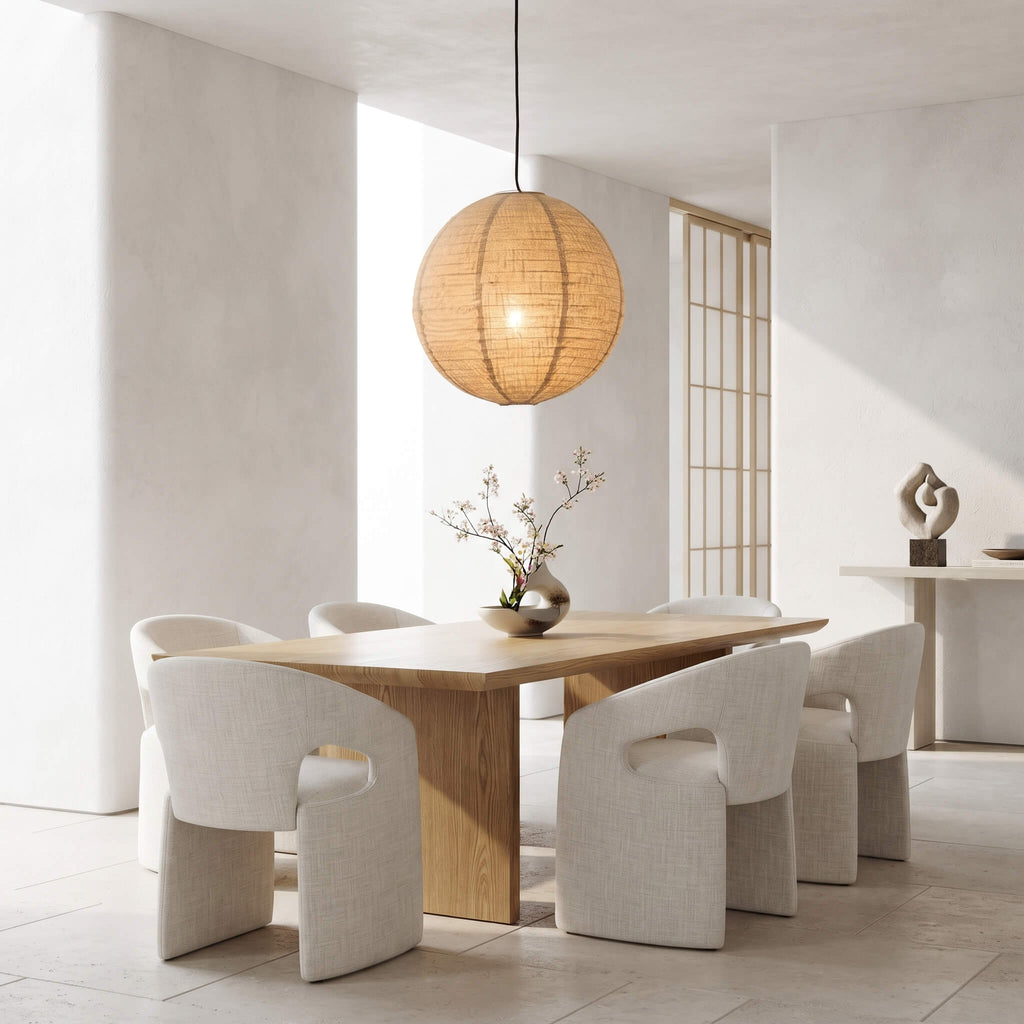 A modern dining room scene with a round woven pendant light hanging above a light wood dining table and six upholstered chairs in a bright, minimalist interior.