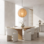 A modern dining room scene with a round woven pendant light hanging above a light wood dining table and six upholstered chairs in a bright, minimalist interior.
