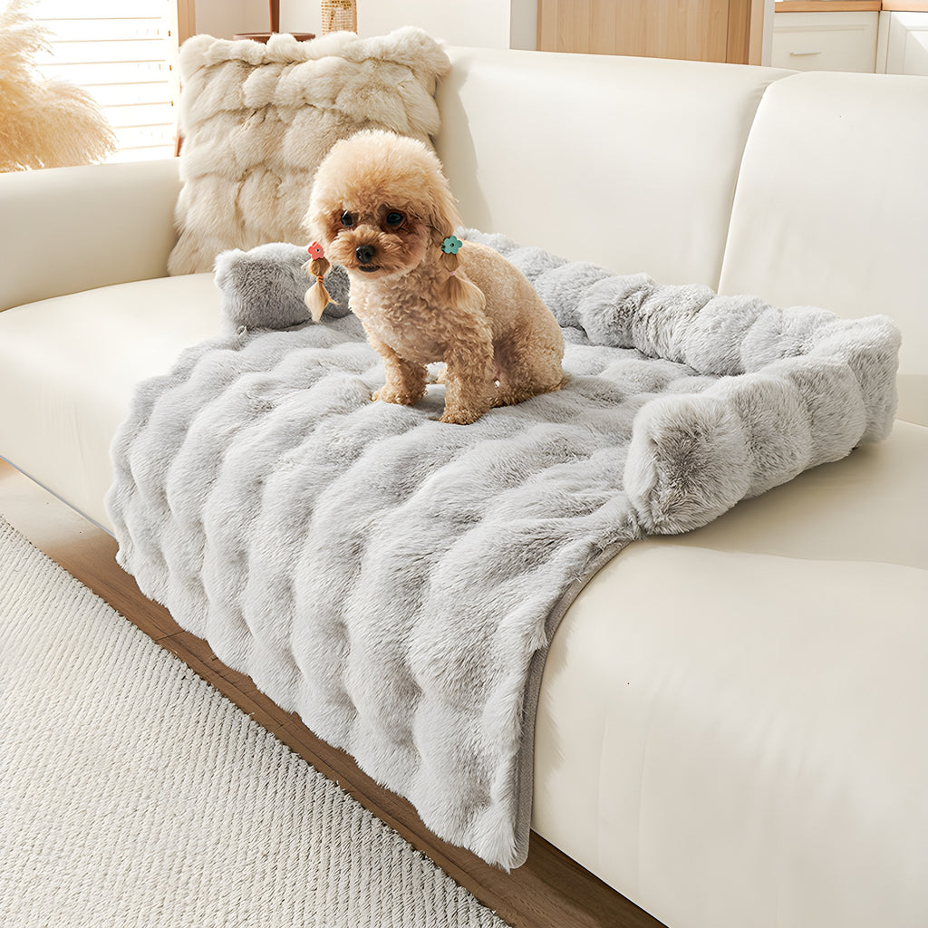 Light grey plush faux fur pet sofa mat on a cream sofa with a small dog sitting on it