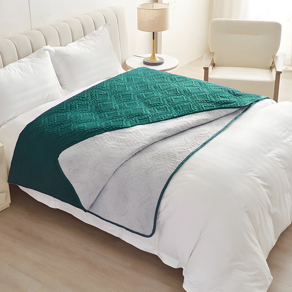 Emerald green quilted waterproof bed cover draped over a white made bed with the light reverse turned back